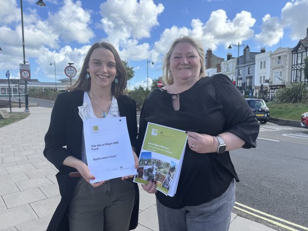 Two women holding funding documents stood on a pavement by a road in Ryde
